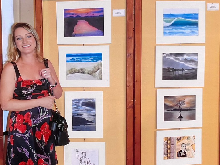 Rebeca Art standing in front of her art displayed at an exhibition in Athens, Greece